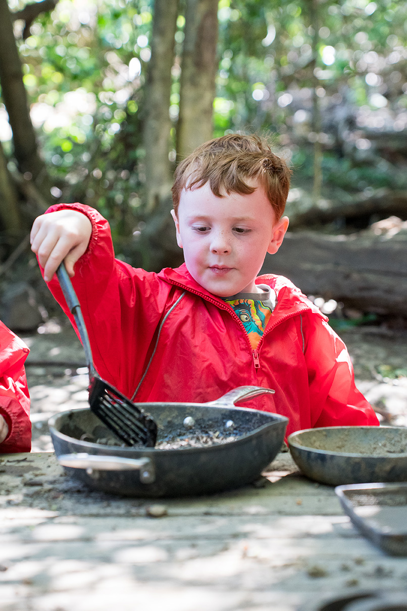 Boy in red waterproofs in forest school