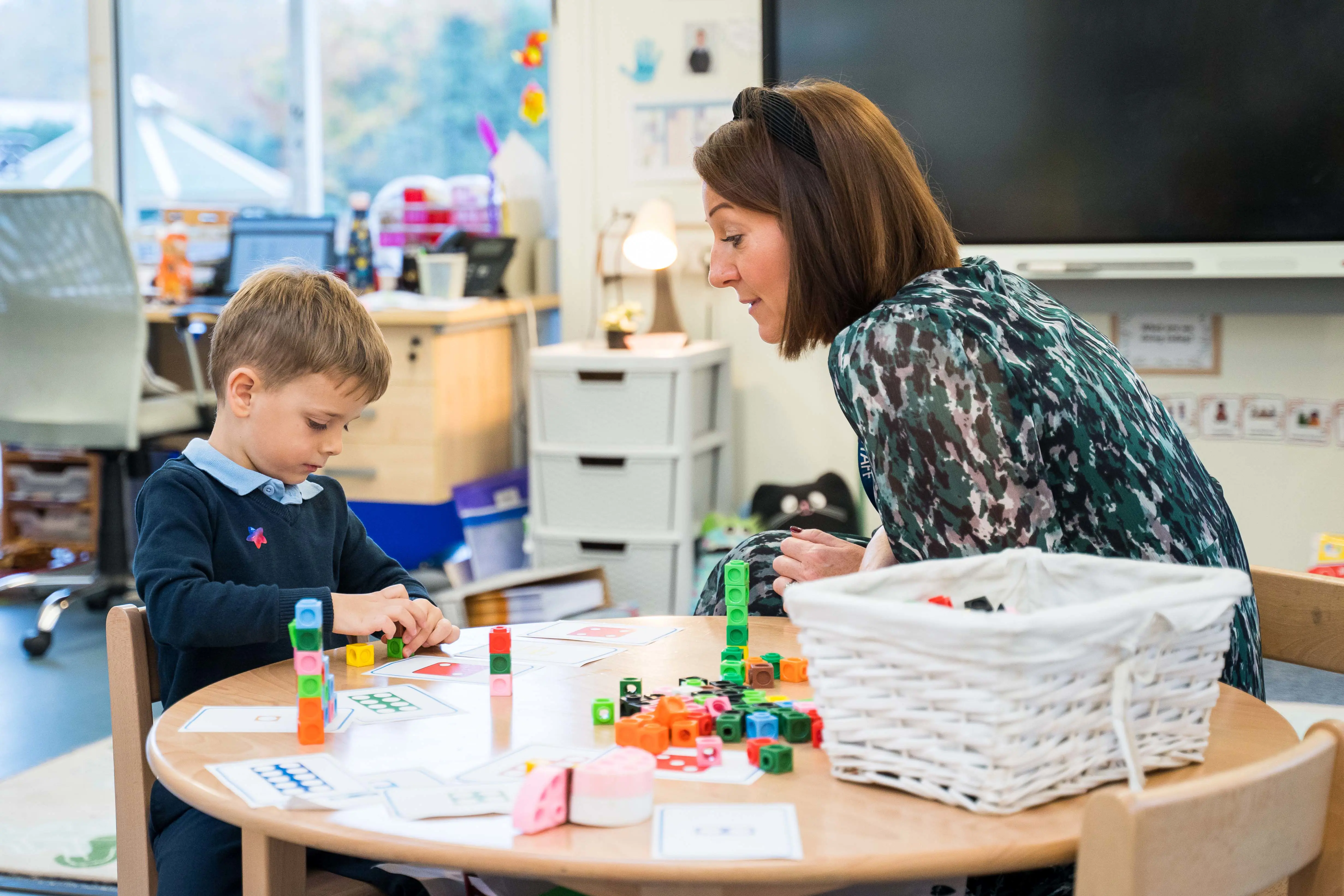 Boy with teacher sitting at a table playing with learning blocks