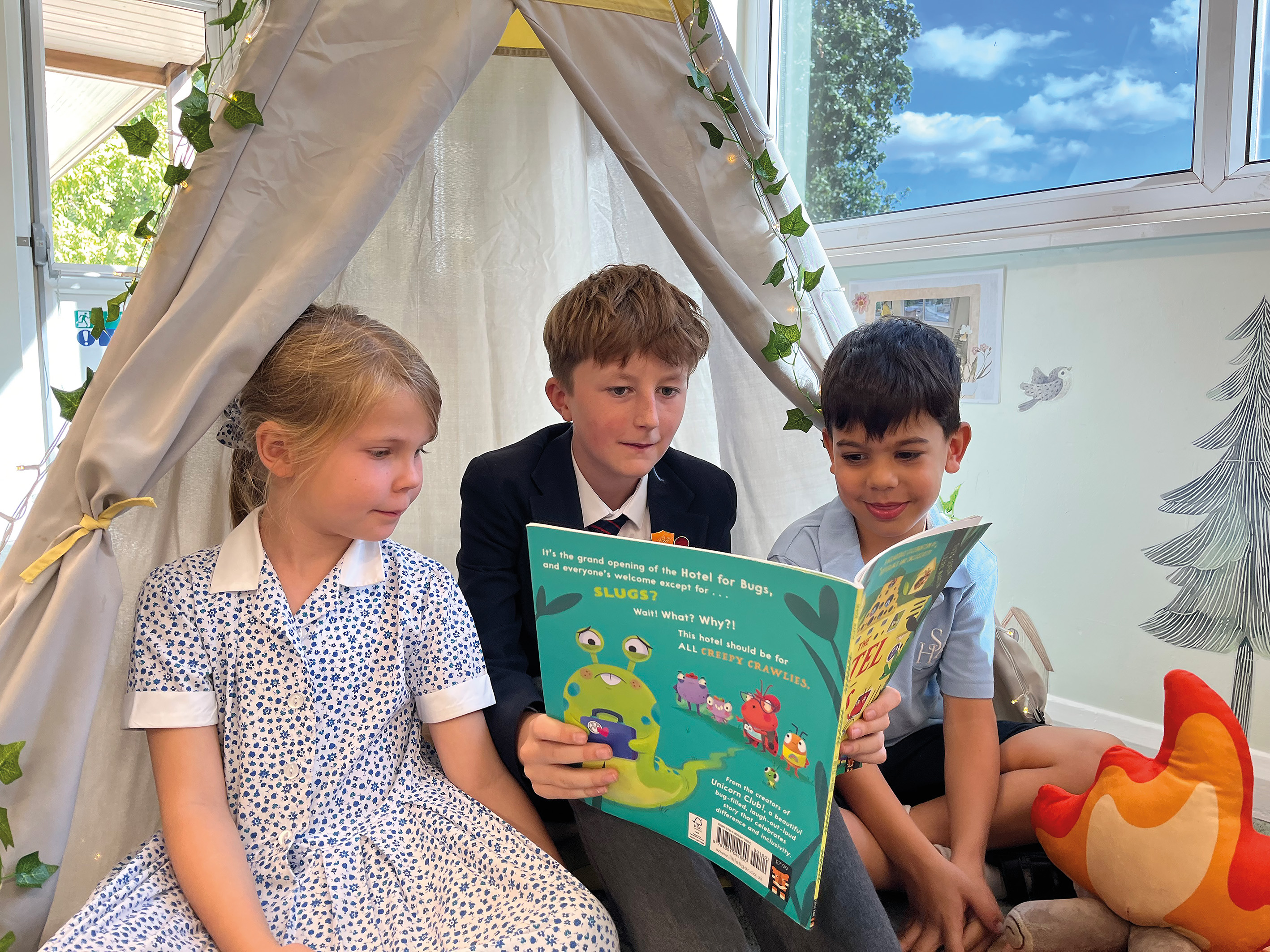 Older pupil reading a book to two younger pupils